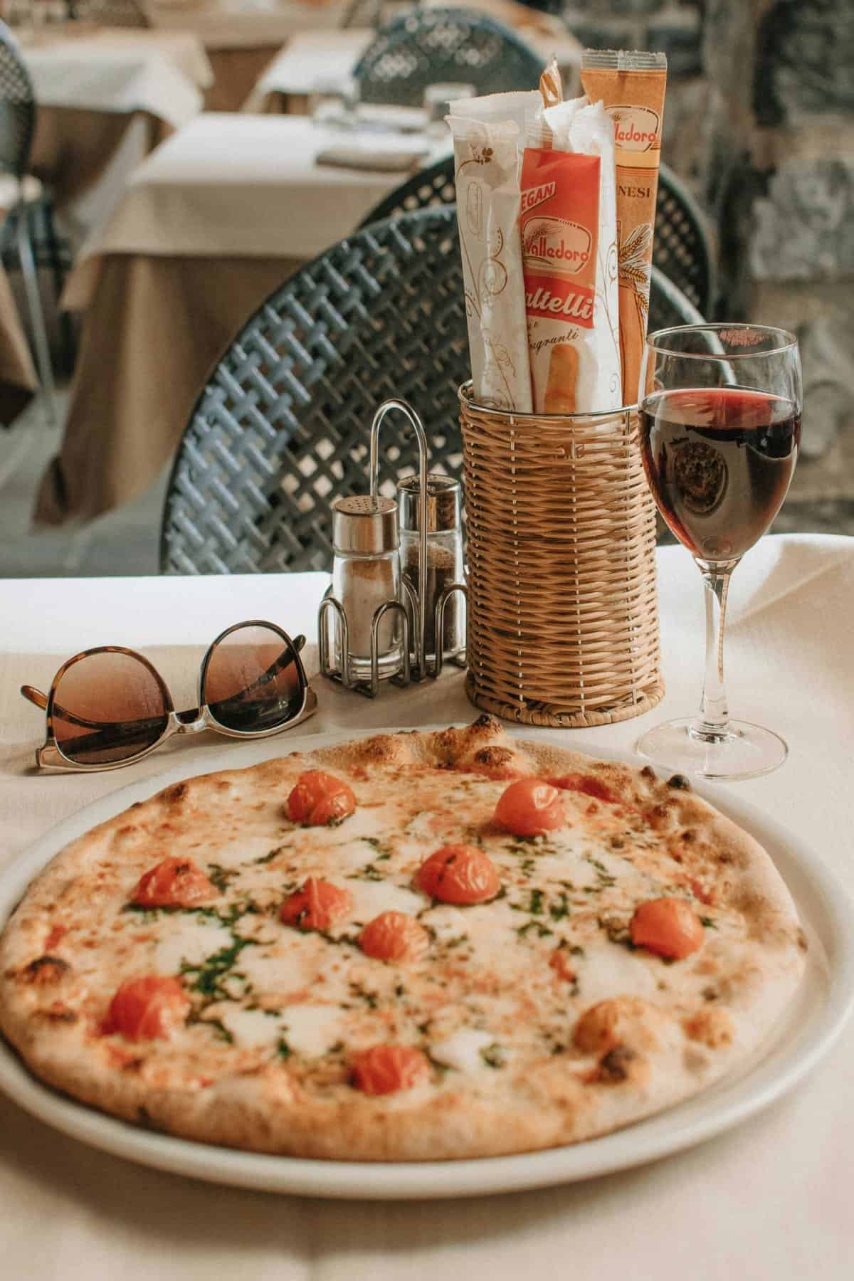 Italian pizza served on an outdoor restaurant terrace with wine.
